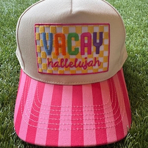 May include: A beige baseball cap with a pink and red striped brim. The front features a rectangular patch with a yellow and white checkered background, embroidered with the word VACAY in multicolored letters and hallelujah in pink script.