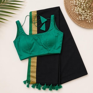 May include: A sleeveless emerald green blouse with a square neckline and thin tie-up straps, paired with a solid black saree featuring a gold border and green tassel fringe along the bottom edge, creating a coordinated two-piece garment set.