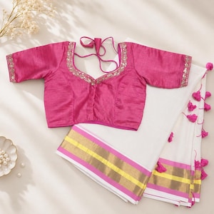 May include: A vibrant fuchsia blouse with short sleeves and intricate silver embroidery along the neckline and cuffs, paired with a white fabric featuring horizontal gold and pink stripes and small pink tassels along the edge.