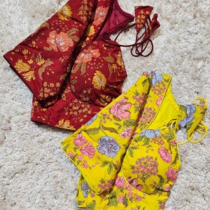 May include: Two floral blouses. One is a deep red with yellow and orange flowers. The other is yellow with pink and blue flowers. Both have a halter-style neckline and are made of a soft fabric.