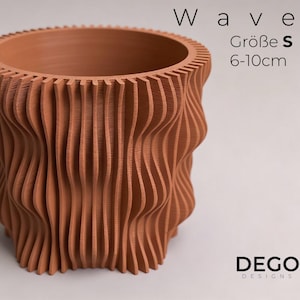 Op de afbeelding: Een terracotta Wave plantenbak met een uniek, gestructureerd ontwerp. De plantenbak heeft een golvend, verticaal patroon en een geribbelde bovenrand. De tekst "Wave" en "Größe S 6-10cm" zijn zichtbaar. Het DEGO DESIGNS logo is ook aanwezig.
