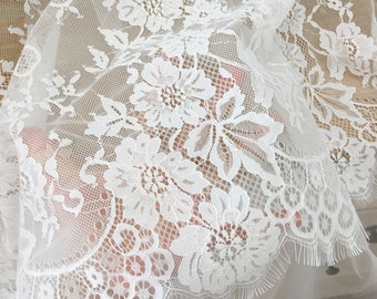 May include: White lace fabric with a delicate floral pattern. The lace has a scalloped edge and is sheer and lightweight.