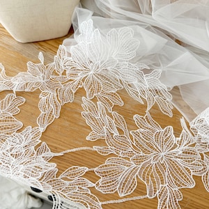 Peut inclure: Garniture en dentelle florale blanche avec un motif délicat. La dentelle est faite d'un tissu en maille fine et présente des motifs floraux complexes. Cette garniture est parfaite pour ajouter une touche d'élégance à tout projet.