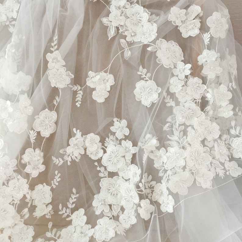 May include: White tulle fabric with white floral embroidery. The embroidery is made of small white beads and pearls. The fabric is sheer and delicate.