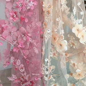 Puede incluir: Dos piezas de tela transparente con bordado floral 3D. La tela de la izquierda es rosa y la tela de la derecha es beige.