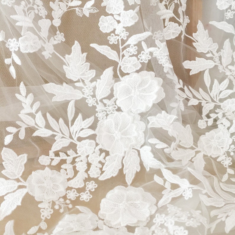 May include: White floral lace fabric with a delicate pattern of flowers and leaves. The lace is on a sheer mesh background.