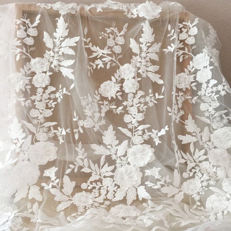 May include: White floral lace fabric with a delicate pattern of flowers and leaves. The lace is on a sheer mesh background.