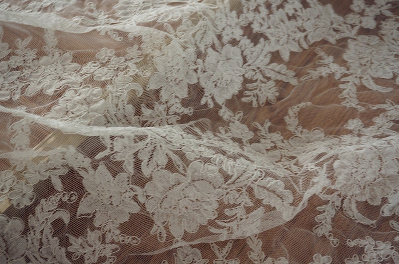 May include: White lace fabric with a floral pattern. The lace is delicate and intricate, with a soft, flowing texture.