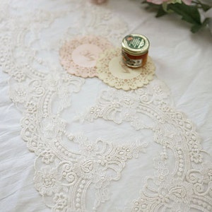Puede incluir: Borde de encaje blanco con un delicado patr&oacute;n floral. El encaje est&aacute; sobre un mantel blanco con dos manteles individuales y un peque&ntilde;o tarro de miel.