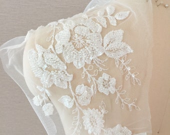 May include: White beaded floral applique on a sheer fabric. The applique features delicate flowers and leaves.