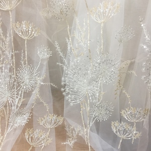 May include: White tulle fabric with silver and gold embroidered floral designs. The fabric has a delicate, airy feel and is perfect for creating a romantic and elegant look.