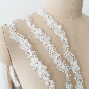 May include: White beaded lace trim with a floral design. The trim is shown on a dress form.