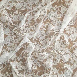 May include: White lace fabric with a delicate floral pattern. The lace is sheer and has a soft, flowing texture.