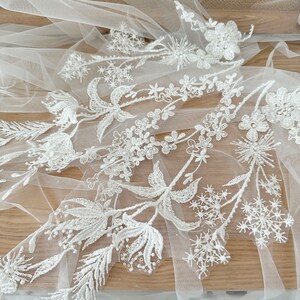 May include: White floral lace applique with delicate beading and a sheer tulle background. This lace trim is perfect for adding a touch of elegance to wedding dresses, bridal accessories, and other craft projects.