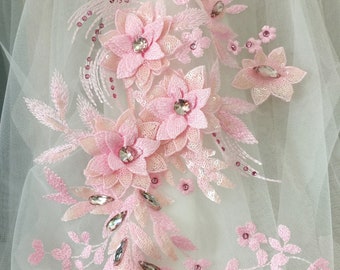 May include: Pink floral applique with sequins and rhinestones. The applique features a cluster of pink flowers with a delicate, intricate design. The flowers are accented with sparkling rhinestones and sequins, adding a touch of glamour to the design.
