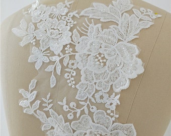 May include: White floral lace applique with sequins. The lace features a delicate floral design with a large central flower and smaller surrounding flowers. The applique is perfect for adding a touch of elegance to any project.