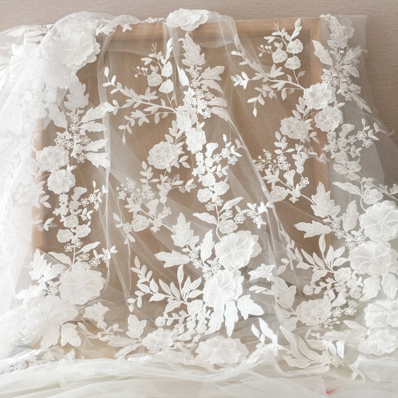 May include: White floral lace fabric with a delicate pattern of flowers and leaves. The lace is on a sheer mesh background.