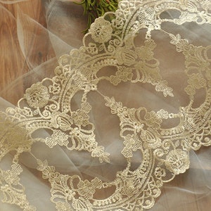 Puede incluir: Borde de encaje dorado con un delicado patr&oacute;n floral sobre una tela blanca transparente.