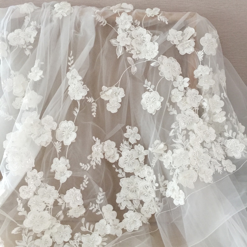 May include: White floral lace fabric with a delicate tulle background. The lace features intricate floral designs with small pearl-like embellishments.