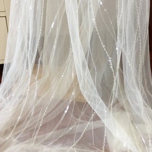May include: White tulle fabric with delicate sequins arranged in diagonal lines. The fabric is sheer and has a soft, flowing texture.