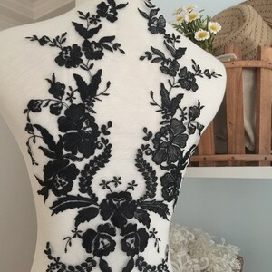 May include: Black floral lace applique for sewing or crafting. The lace features delicate flowers and leaves on a sheer mesh background.