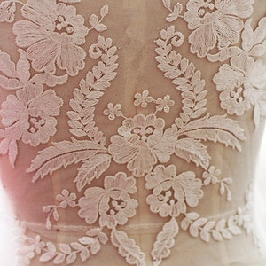 May include: White floral lace applique with delicate embroidery. The lace features a floral design with leaves and branches. This lace applique is perfect for adding a touch of elegance to any project.
