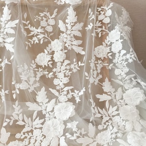 May include: White floral lace fabric with a delicate pattern of flowers and leaves. The lace is on a sheer, white mesh background.