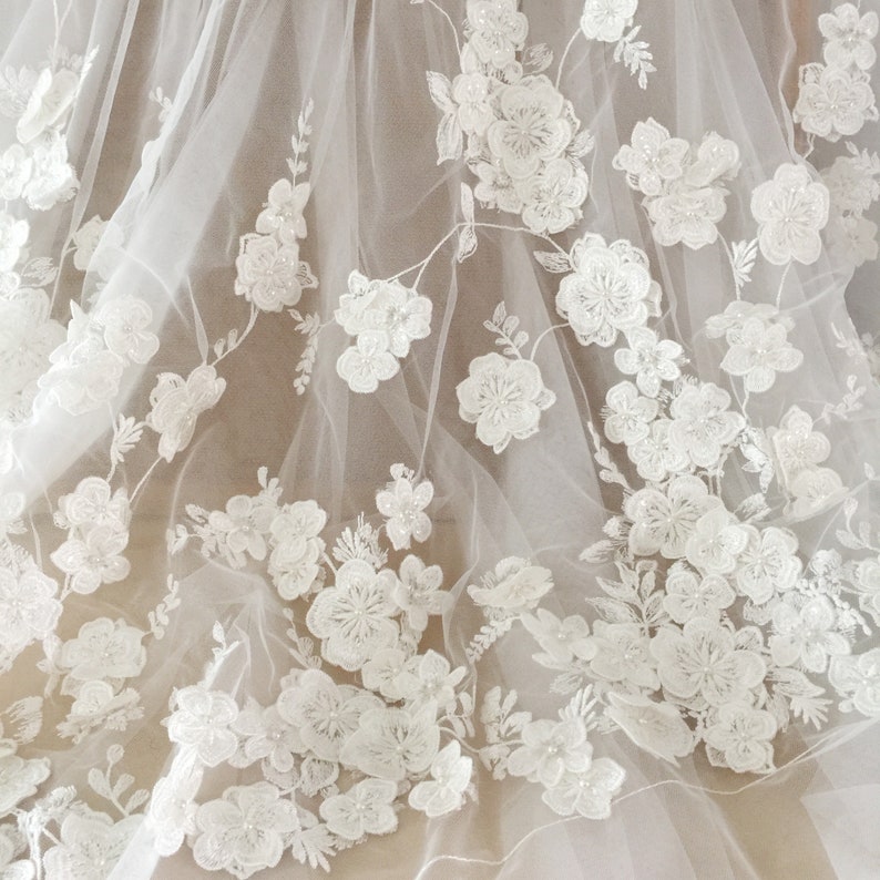 May include: White floral lace fabric with a delicate, intricate design. The lace features small, white flowers and leaves, with a subtle shimmer.