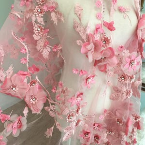 Puede incluir: Tela de encaje floral rosa con flores 3D y pedrer&iacute;a. La tela es transparente y delicada, con un aspecto suave y femenino.
