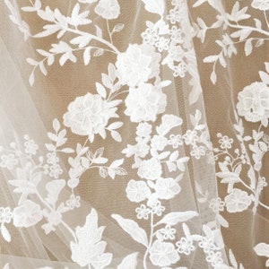 May include: White floral lace fabric with a delicate pattern of flowers and leaves. The lace is sheer and has a soft, romantic look.
