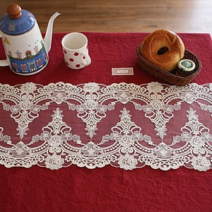 Puede incluir: Borde de encaje blanco con un delicado patr&oacute;n floral, colocado sobre un mantel rojo con una tetera, una taza y un pastel.