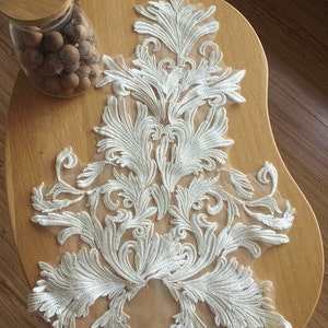 May include: White lace applique featuring a floral design. The lace is delicate and intricate, with a variety of different shapes and sizes of flowers. The applique is ideal for adding a touch of elegance to any project.