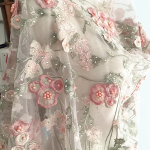 May include: Pale pink and green floral embroidery on a sheer white fabric with iridescent rhinestones. The fabric is delicate and has a soft, feminine feel.