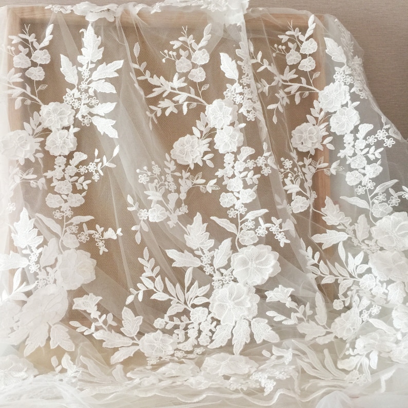 May include: White floral lace fabric with a delicate pattern of flowers and leaves. The lace is on a sheer, ivory background.