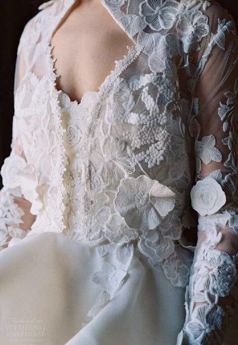 May include: A white lace wedding dress with a high neckline and long sleeves. The dress is adorned with delicate floral embroidery and 3D floral appliques.