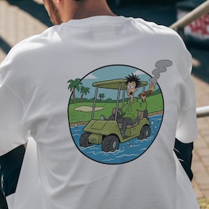 May include: White t-shirt with a circular graphic on the back featuring a cartoon golf cart in water. The cart has a person smoking a cigar. The background includes palm trees and a golf course.