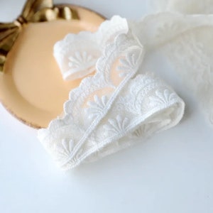 May include: White lace trim with a delicate floral pattern. The lace is soft and has a scalloped edge.
