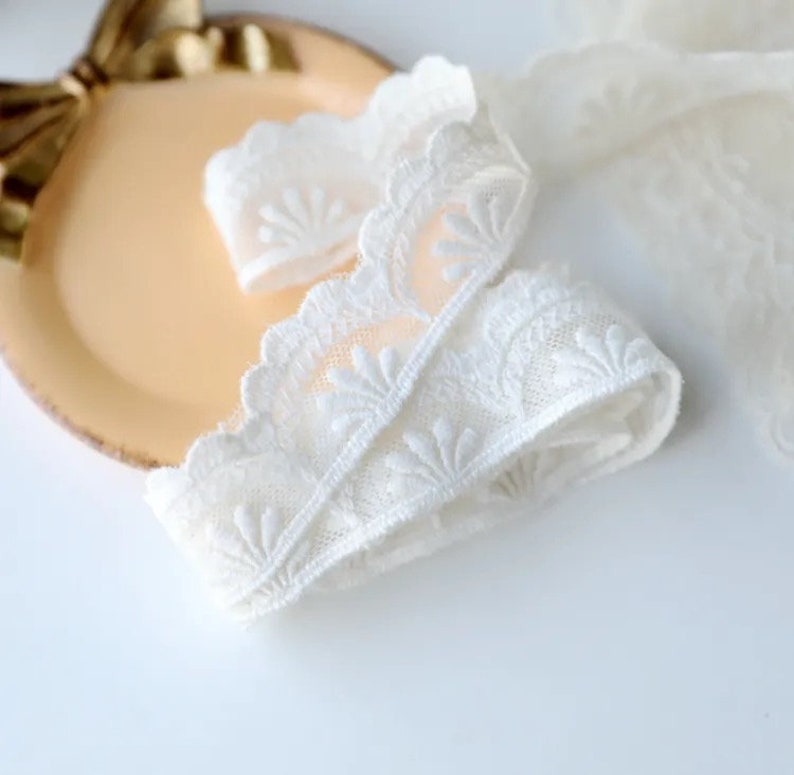 May include: White lace trim with a delicate floral pattern. The lace is soft and has a scalloped edge.