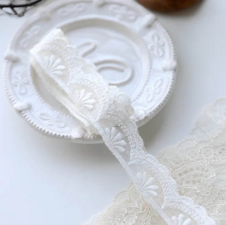 May include: White lace trim with a scalloped edge and floral design. The lace is delicate and intricate, with a soft, feminine feel.