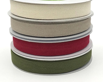 May include: Four spools of cotton twill tape in different colors: natural, beige, red, and olive green. The tape is woven in a herringbone pattern.