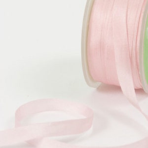 May include: A spool of pale pink satin ribbon. The ribbon is thin and delicate, and it is wound around a white spool.