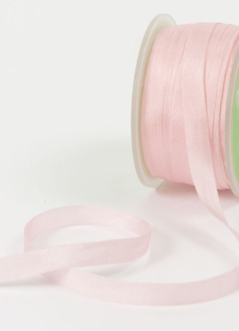 May include: A spool of pale pink satin ribbon. The ribbon is thin and delicate, and it is wound around a white spool.