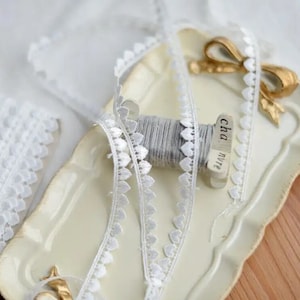 May include: White lace trim with heart-shaped embellishments, wound around a spool of thread. The spool is labeled "cha. nyve".