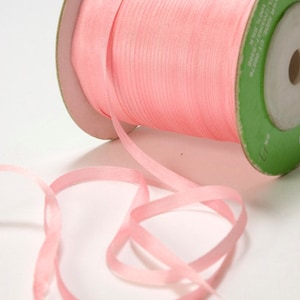 May include: A spool of pink satin ribbon. The ribbon is wound around a cardboard spool with a green label. The ribbon is approximately 1/4 inch wide.