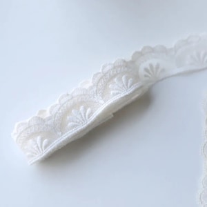 May include: White lace trim with a scalloped edge and a delicate floral pattern.