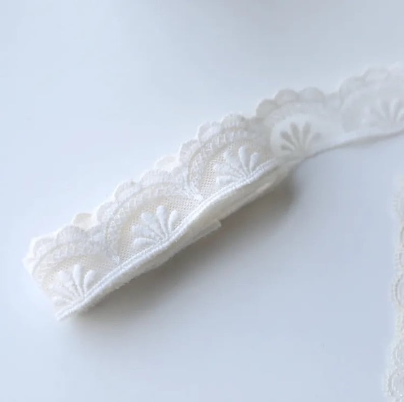 May include: White lace trim with a scalloped edge and a delicate floral pattern.