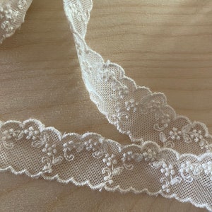 May include: White lace trim with a delicate floral pattern. The lace is soft and has a scalloped edge.