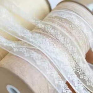 Puede incluir: Carretes de cinta de encaje blanca con delicados motivos florales. La cinta está enrollada alrededor de carretes de cartón.