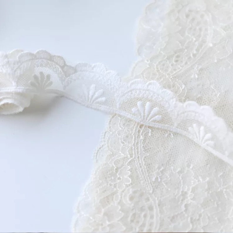 May include: White lace trim with a scalloped edge and delicate floral designs. The lace is soft and sheer, perfect for adding a touch of elegance to any project.