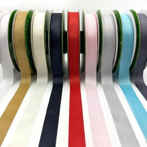 May include: Ten spools of ribbon in various colors, including white, beige, navy blue, red, pink, gray, light blue, and dark gray. The ribbon is arranged in a row, with the spools facing the viewer.